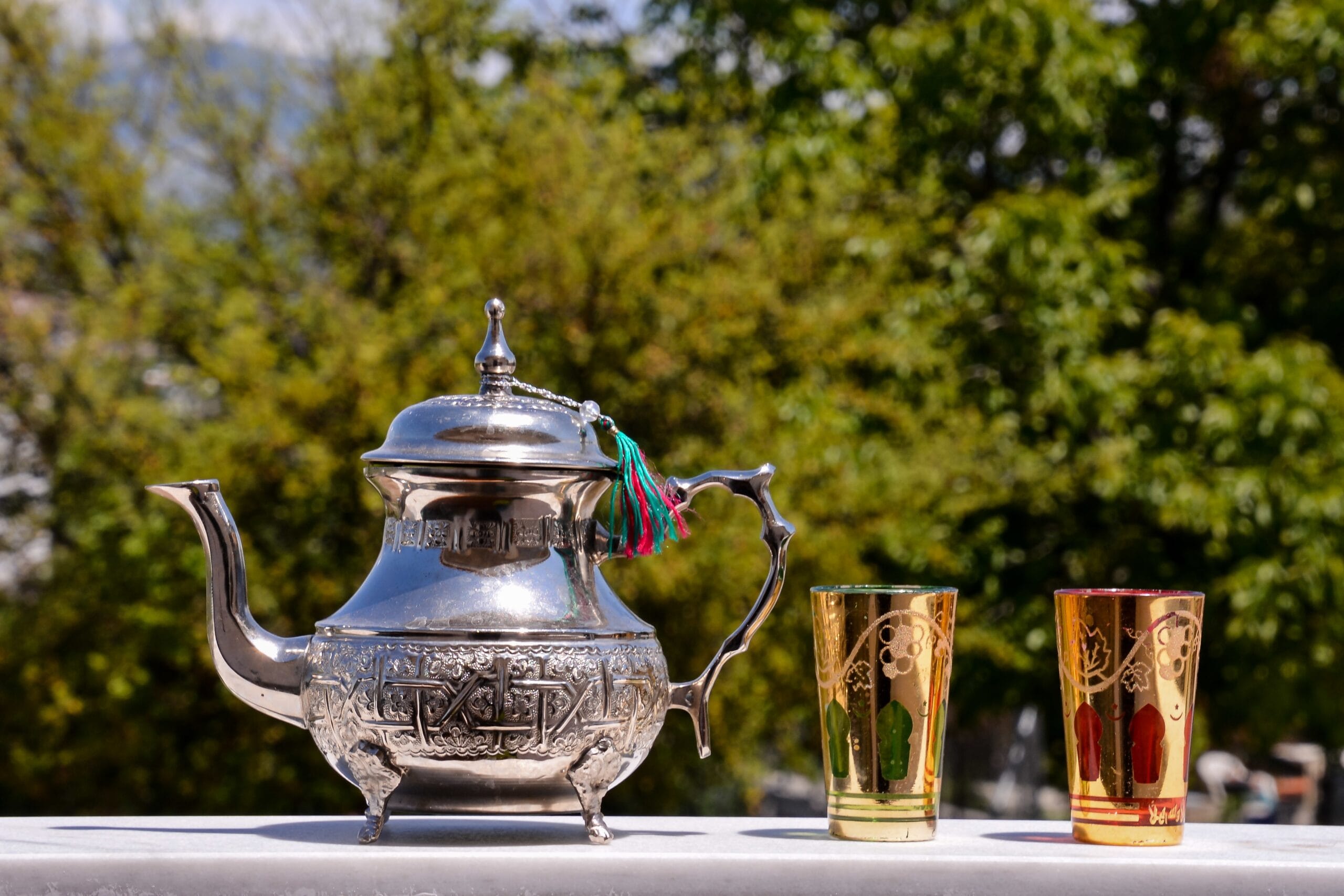 A traditional Moroccan tea set with a silver teapot, ornate tray, and glasses filled with mint tea, garnished with fresh mint leaves.