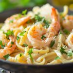Creamy shrimp pasta with golden seared shrimp, garlic butter sauce, parmesan, and parsley on a rustic table.